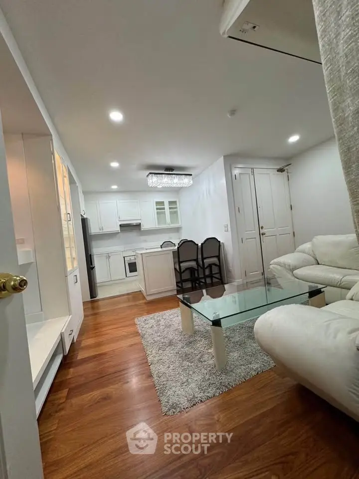 Modern living room with open kitchen, hardwood floors, and elegant white furniture.