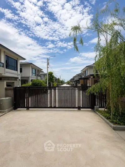 Gated entrance to modern residential community with clear blue sky and lush greenery.