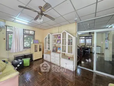 Spacious living room with wooden flooring and ceiling fan, featuring large windows and built-in cabinets.