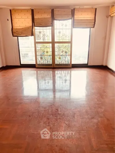 Spacious sunlit room with polished wooden floors and large windows.