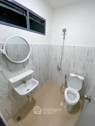 Modern bathroom with sleek fixtures and marble wall tiles, featuring a round mirror and compact design.