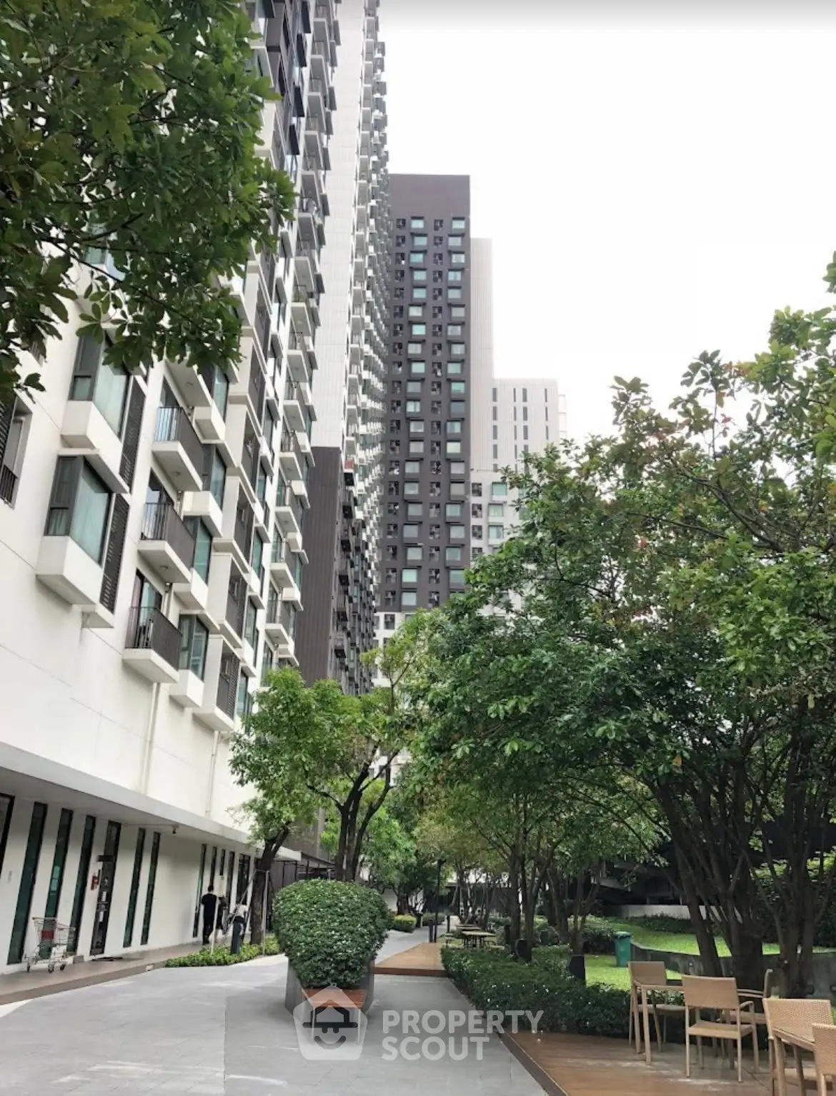 Modern high-rise building with lush garden and outdoor seating area.