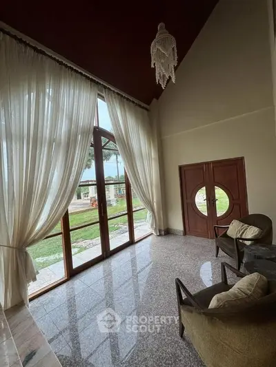 Elegant living room with high ceilings, large windows, and stylish decor overlooking a lush garden.
