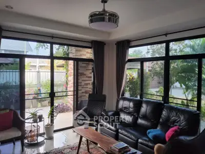 Spacious living room with large windows and garden view, featuring modern furniture and natural light.