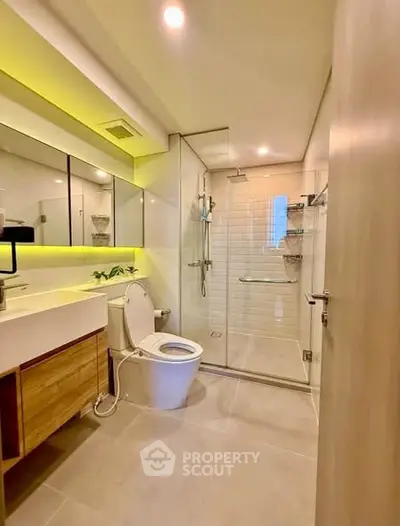 Modern bathroom with glass shower, sleek vanity, and ambient lighting.
