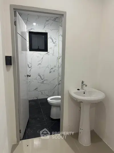 Modern bathroom with sleek pedestal sink and marble-tiled walls, offering a clean and contemporary design.