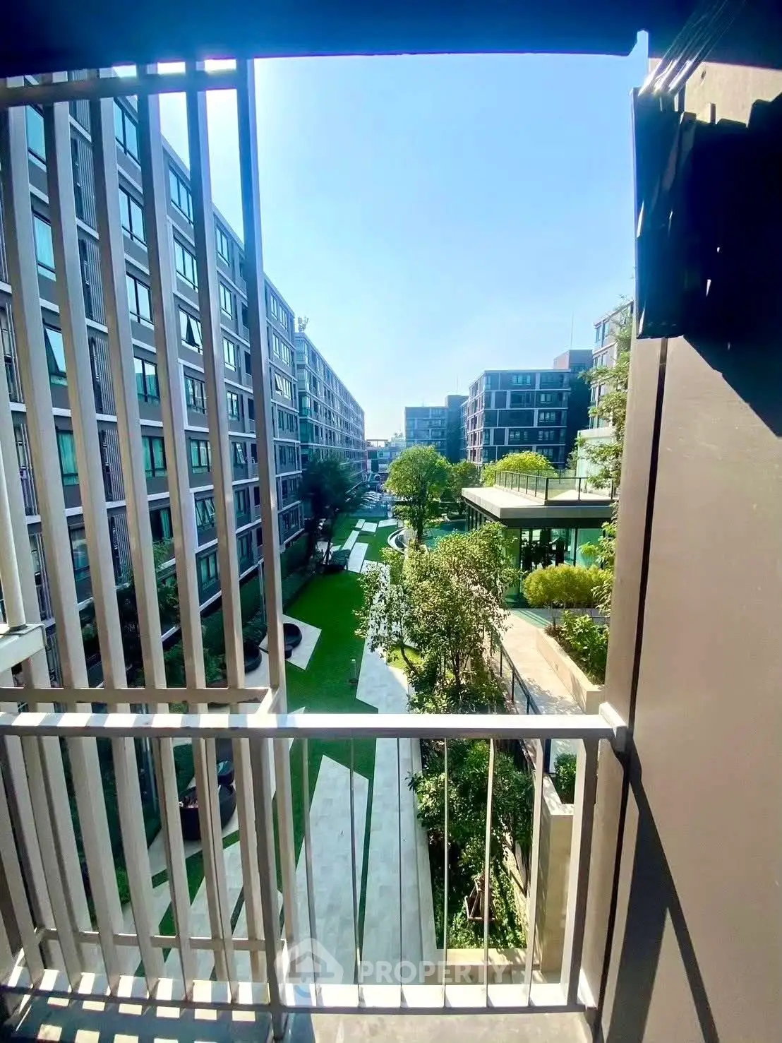 Modern apartment view with lush garden and sleek architecture from balcony.