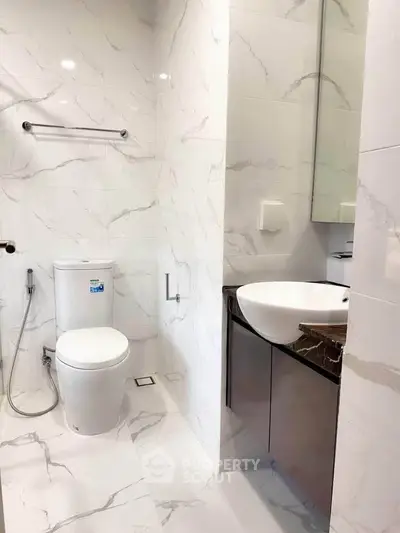Modern bathroom with sleek fixtures and marble tiles, featuring a stylish sink and toilet.
