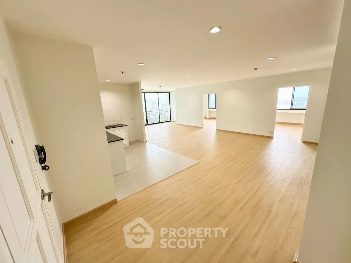 Spacious open-plan living area with wooden flooring and large windows offering city views.