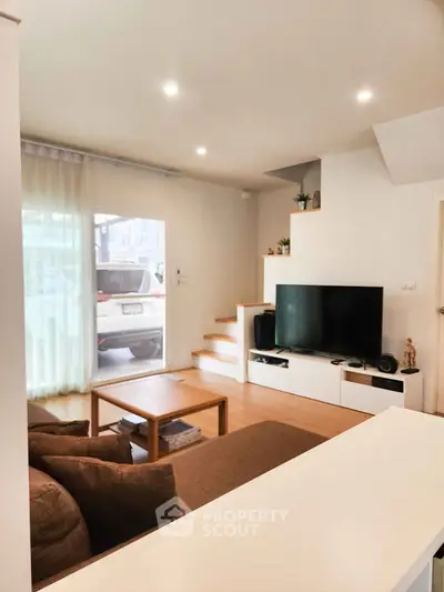 Modern living room with cozy brown sofa, wooden coffee table, and sleek TV setup near large window.