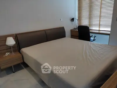 Modern bedroom with sleek furniture and natural light from large window blinds.