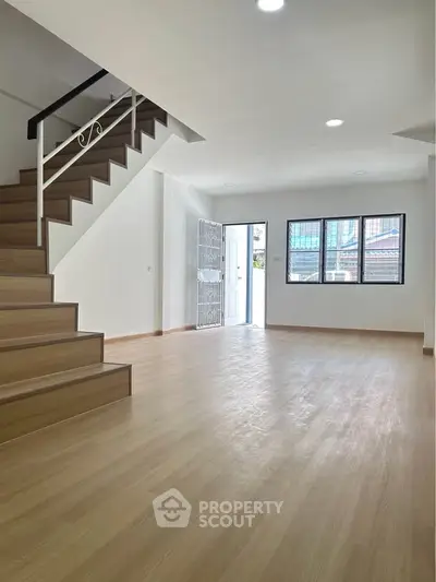 Spacious open-plan living room with wooden flooring and staircase, perfect for modern living.