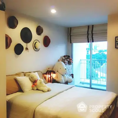 Cozy bedroom with stylish hat wall decor and plush toys, leading to a balcony with a view, perfect for relaxation and comfort.