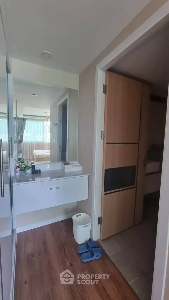 Modern bathroom with sleek vanity and wooden flooring, offering a glimpse into a bright living area.