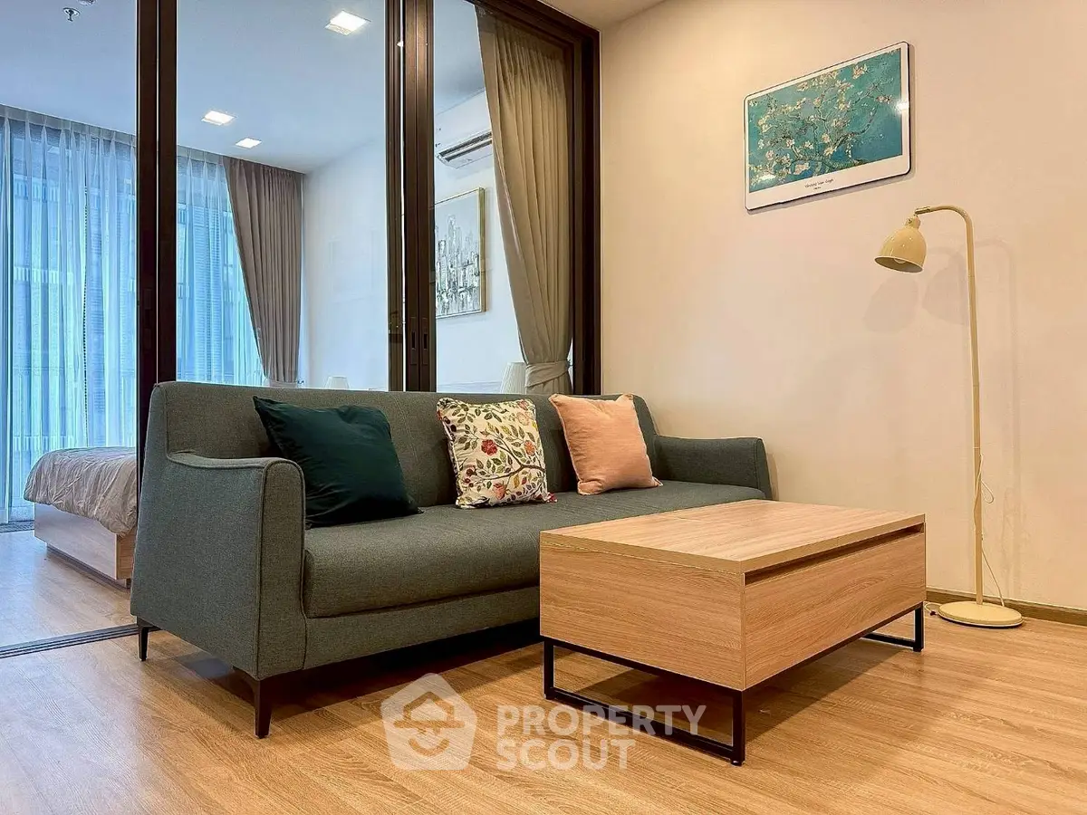 Modern living room with stylish sofa and coffee table, adjacent to a cozy bedroom with glass partition.