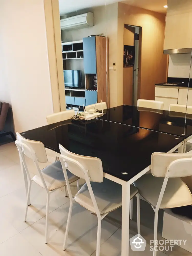 Modern dining area with sleek black glass table and white chairs in stylish apartment.