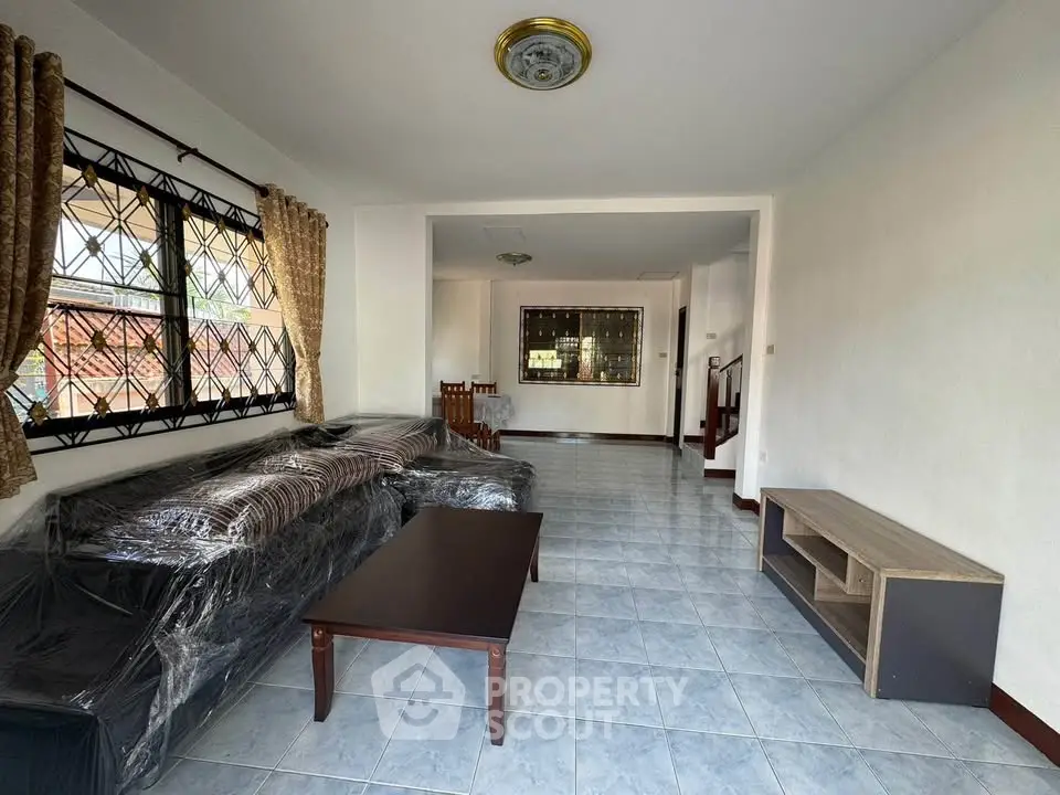Spacious living room with tiled flooring and natural light, featuring a cozy sofa and elegant curtains.