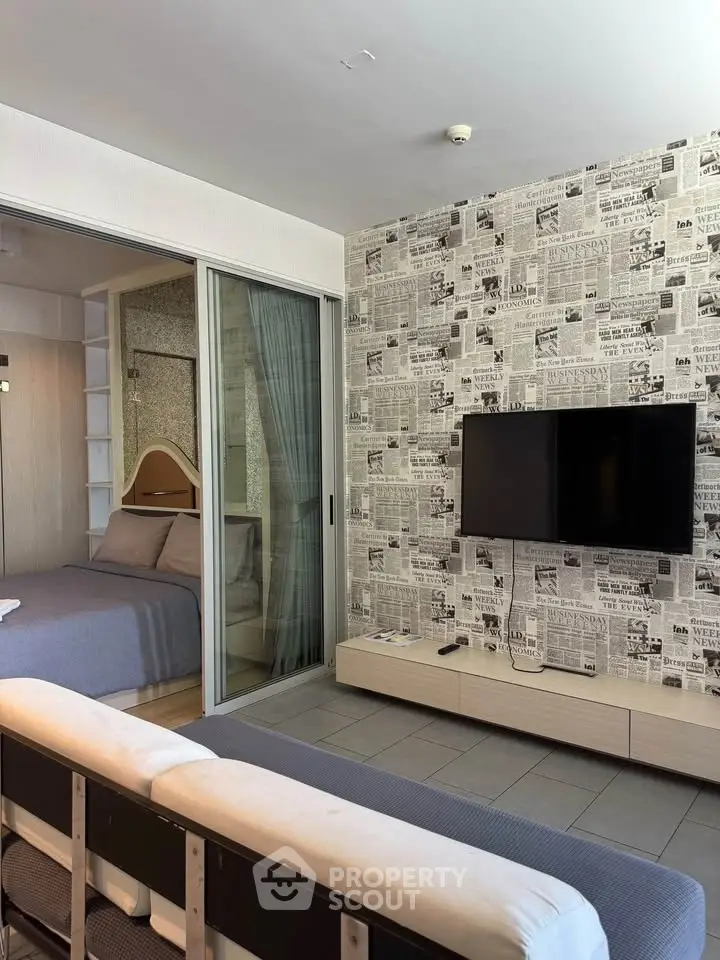 Modern living room with stylish newspaper wallpaper and wall-mounted TV, adjacent to cozy bedroom with sliding glass doors.