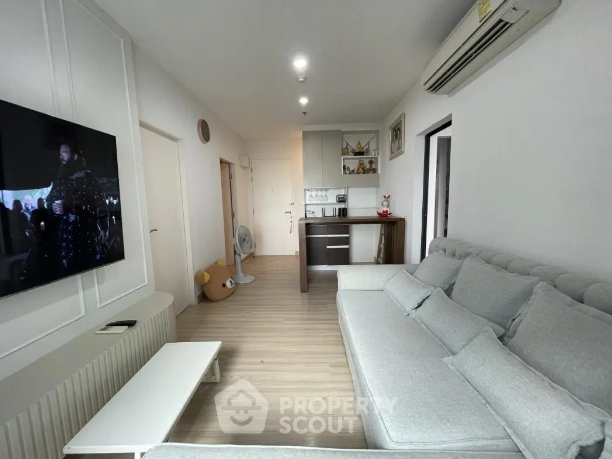 Modern living room with cozy sofa and wall-mounted TV, open layout to kitchen area.