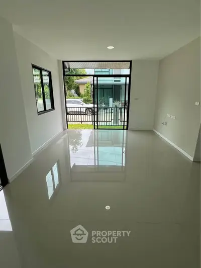 Spacious modern living room with large windows and glossy floors, offering a bright and inviting atmosphere.