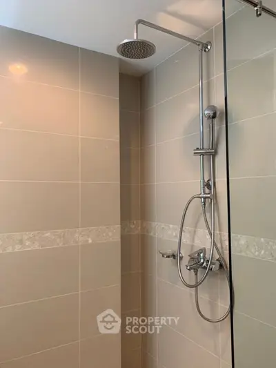 Modern bathroom shower with sleek fixtures and beige tiled walls.