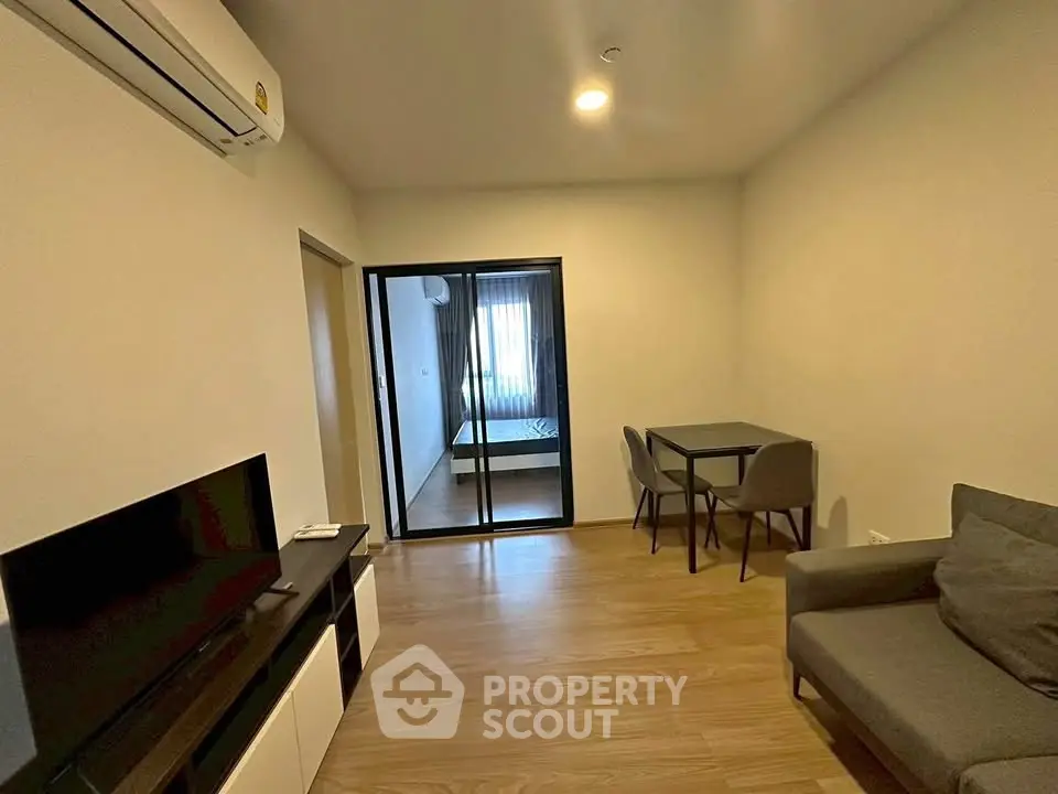 Modern living room with sleek furniture and open layout, featuring a cozy dining area and a glimpse into the bedroom.