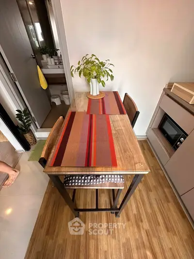 Cozy dining area with wooden table, vibrant placemats, and modern kitchen setup in a compact apartment.