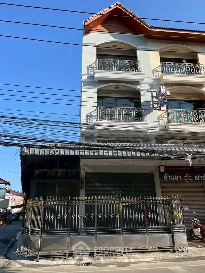 Charming three-story building with ornate balconies and gated entrance in vibrant urban setting.