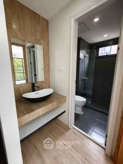 Modern bathroom with stylish sink and wooden accents, featuring a sleek shower area.