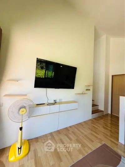 Modern living room with wall-mounted TV, wooden flooring, and minimalist decor