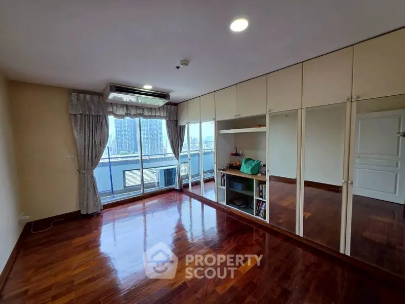 Spacious bedroom with mirrored closets and city view balcony in modern apartment.