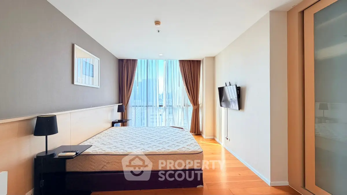 Spacious bedroom with large window and city view, featuring modern decor and hardwood floors.
