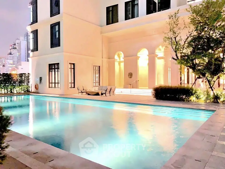 Luxurious apartment building with illuminated pool and elegant architecture at dusk.