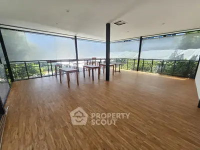 Spacious sunlit room with wooden flooring and large windows offering serene views.
