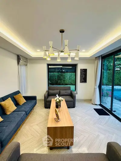 Elegant living room with modern chandelier and garden view, featuring stylish furniture and large windows.