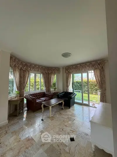 Spacious living room with elegant decor and garden view, featuring large windows and stylish furniture.