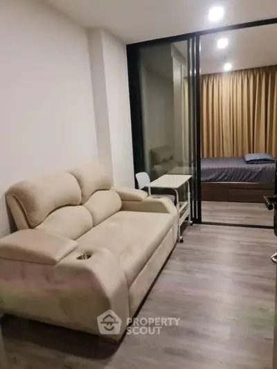 Modern apartment with cozy living room and bedroom separated by glass partition, featuring stylish furnishings.