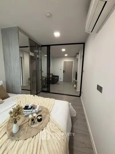 Modern bedroom with stylish decor and glass partition leading to living area, featuring cozy bedding and sleek design.