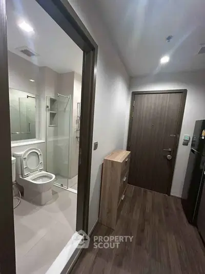 Modern apartment entrance with adjacent bathroom featuring sleek design and wooden flooring.