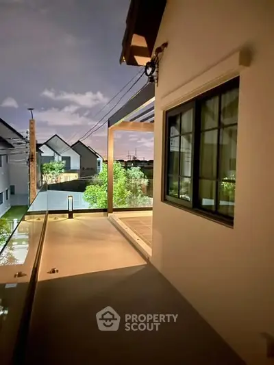Modern balcony with glass railing and night view of contemporary houses.