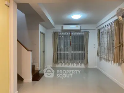 Spacious living room with staircase and large window, featuring modern air conditioning.