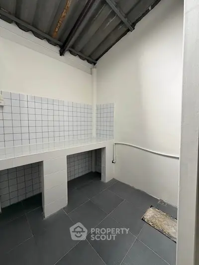 Spacious utility area with tiled walls and flooring, ideal for laundry or storage use.