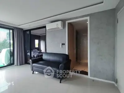 Modern apartment interior with sleek black sofa and air conditioning, featuring a glimpse into a cozy bedroom.