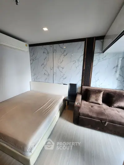 Modern bedroom with marble accent wall and cozy seating area in a stylish apartment.
