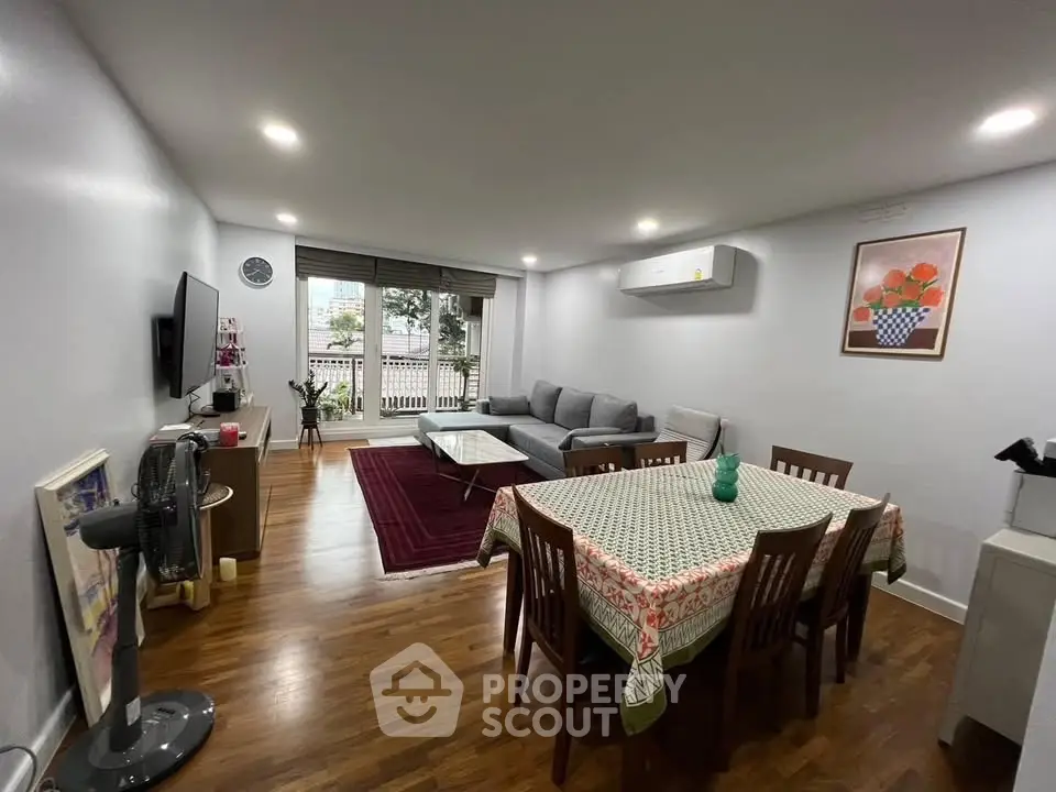 Spacious living room with modern decor and dining area, featuring hardwood floors and natural light.