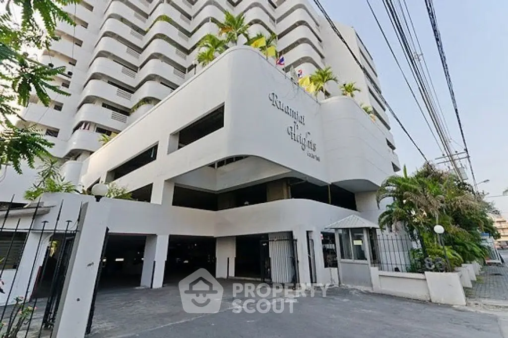Modern high-rise building exterior with palm trees and spacious parking area.