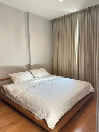 Cozy bedroom with wooden flooring and large window with curtains, featuring a comfortable double bed.
