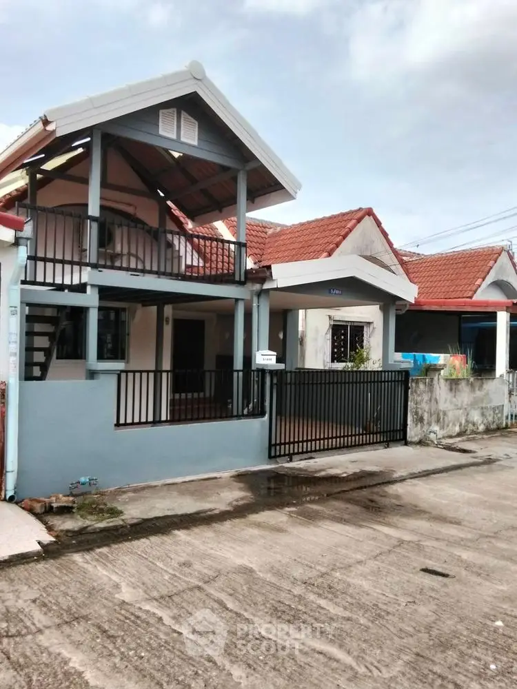 Charming two-story house with red roof and gated entrance in a quiet neighborhood.