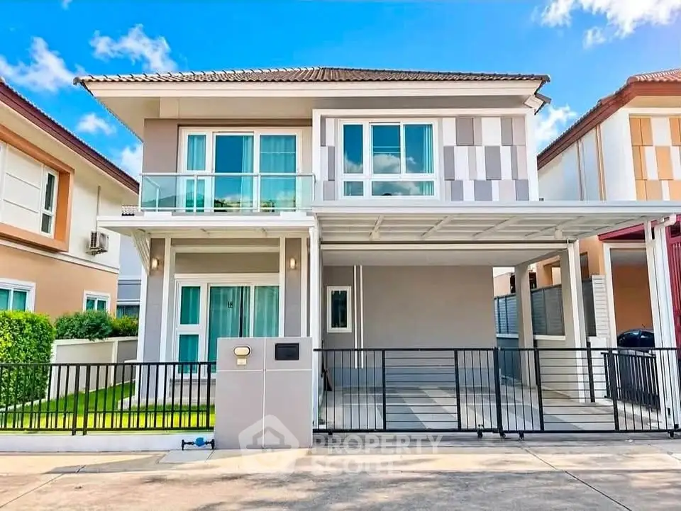 Modern two-story house with balcony and gated driveway in a suburban neighborhood.