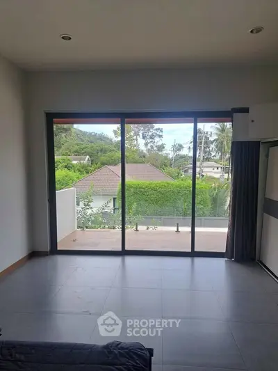 Spacious living room with large windows offering a scenic view of lush greenery and a private balcony.